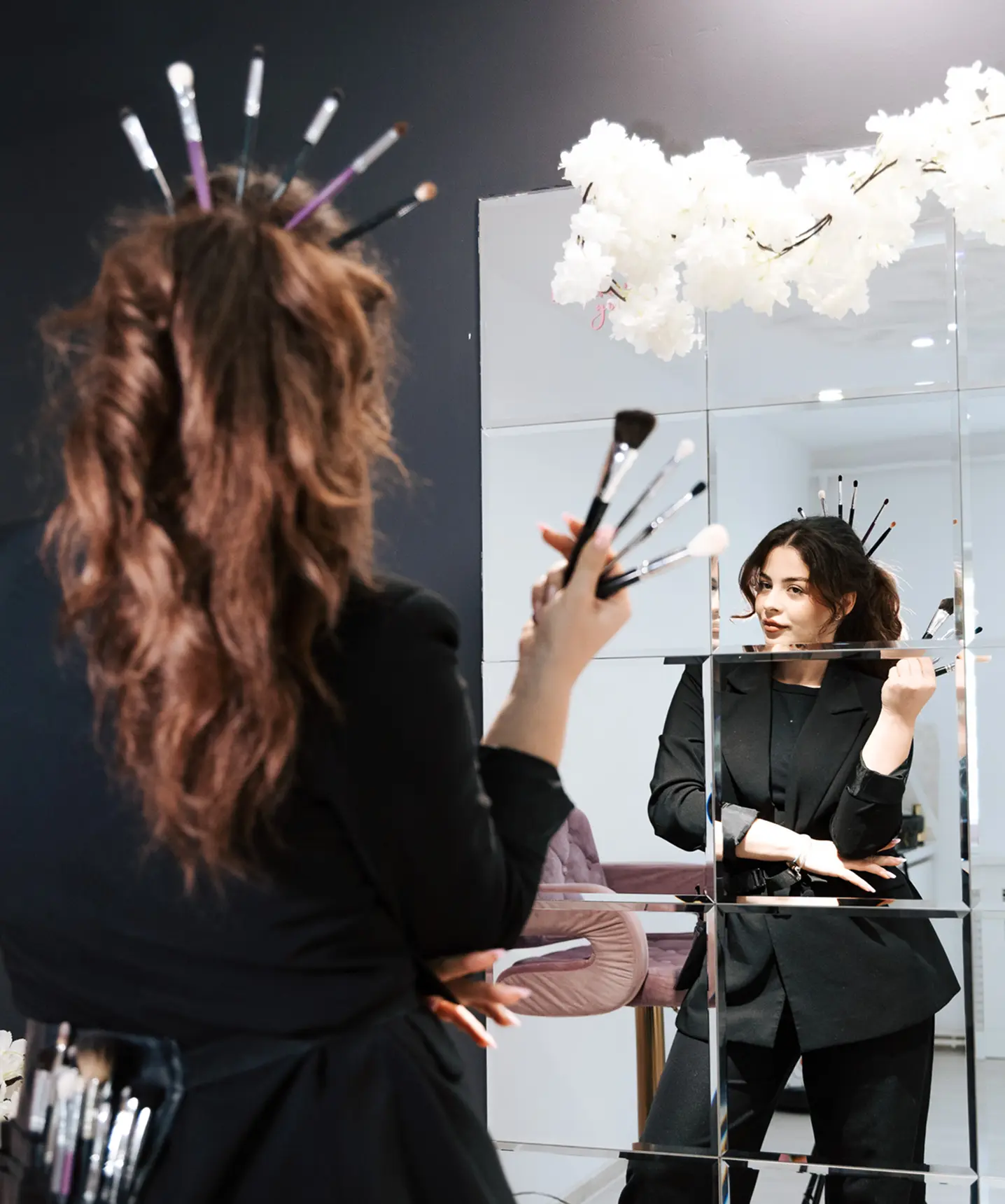 Reflexie creativă a makeup artistei în oglindă, cu pensule în mână, în păr și la brâu